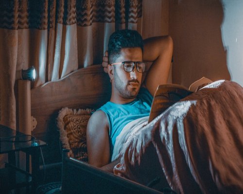Person reading a book in bed with a warm directional reading lamp